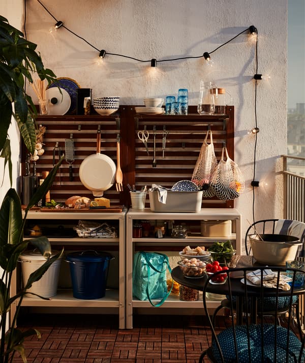 A simple outdoor kitchen at one end of a balcony, with shelves, wall panels, LED lights and utensils.