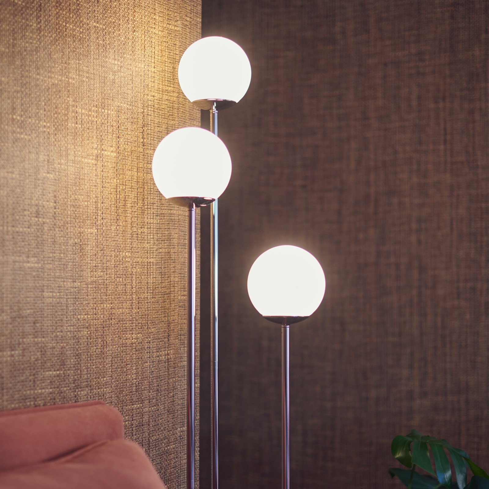 A SIMRISHAMN floor lamp with three bulbs giving off a warm glow against natural brown walls in the coer of a living room.