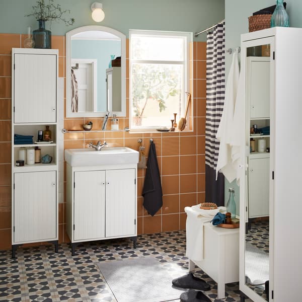 A sink cabinet and a tall storage cabinet with white paneled cabinet doors in a bathroom with orange wall tiles.