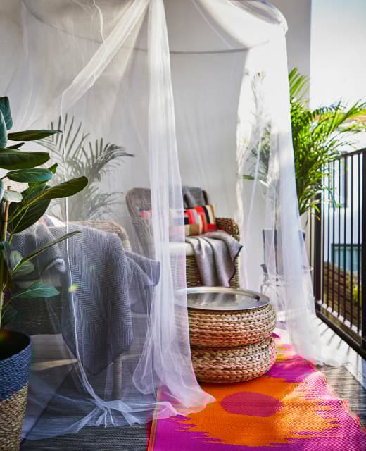 A sitting area with two cozy armchairs and a small table are given privacy with a canopy hung above.