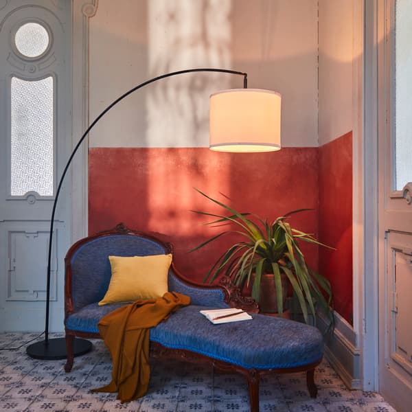 A SKAFTET arched floor lamp base with a white lampshade providing overhead lighting in a corner above a divan.