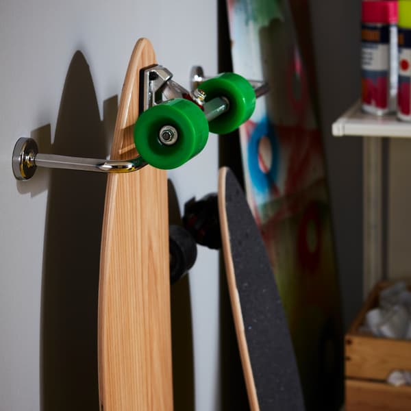 A skateboard hanging from a chrome effect IKEA VOXNAN towel rail attached to a wall.