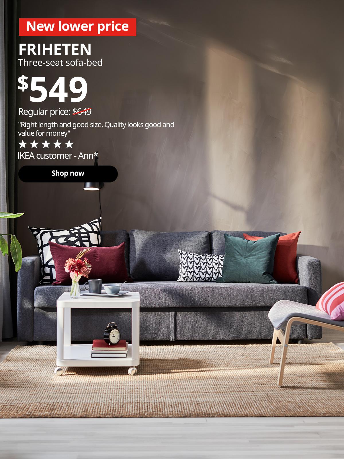 A Skiftebo dark grey FRIHETEN 3-seat sofa-bed in a living room setting. In the top left corner, a red tag with white text reads 'New lower price'. Accompanying white text displays: 'FRIHETEN, Three-seat sofa-bed, $549, Regular price: $649'