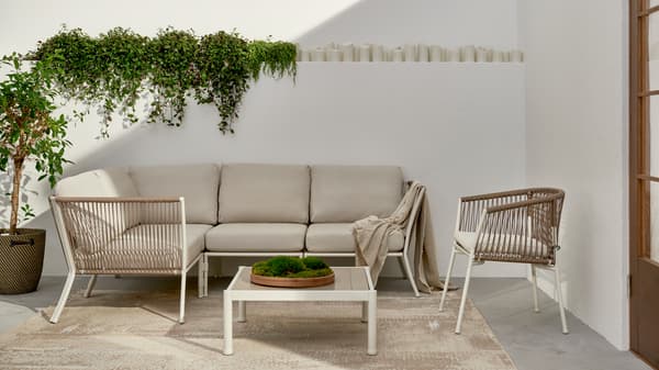 A sleek and serene patio setup with a beige cushioned sectional sofa, two light wicker armchairs, and a modern white coffee table – creating a minimalist and inviting outdoor lounge.