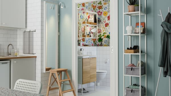 A sliding door opens up from the kitchen to a colourful bathroom with floral wallpaper and a small washstand.