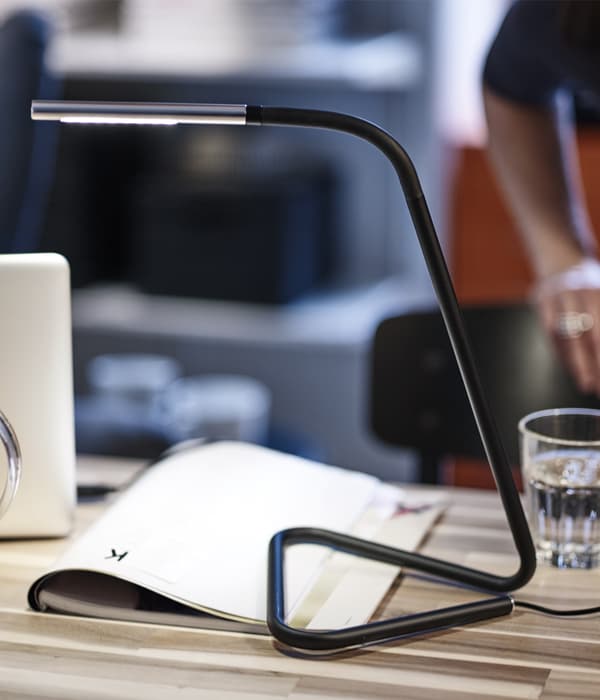 A slim black work light on a table with a glass and book on it.