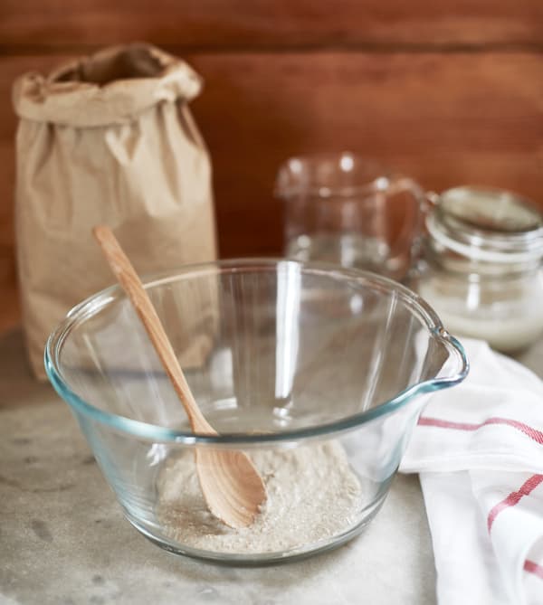 A small amount of sourdough starter is in a glass bowl with a wooden spoon. 