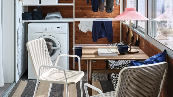 A small balcony with a white storage system for laundry, a washing machine, a small table and two white/beige chairs.