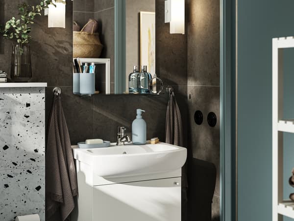 A small bathroom with dark brown walls and white furniture. A NYSJÖN cabinet with one door holds storage under the sink.