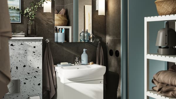 A small bathroom with dark brown walls and white furniture. A NYSJÖN cabinet with two doors holds storage under the sink.