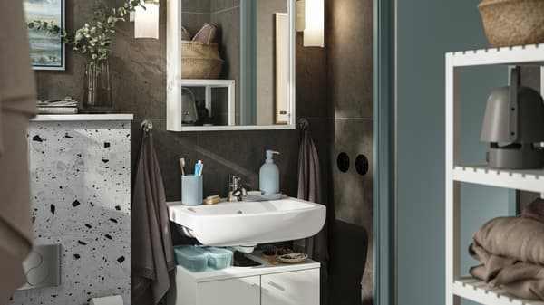 A small bathroom with dark brown walls and white furniture. A NYSJÖN cabinet with two doors holds storage under the sink.