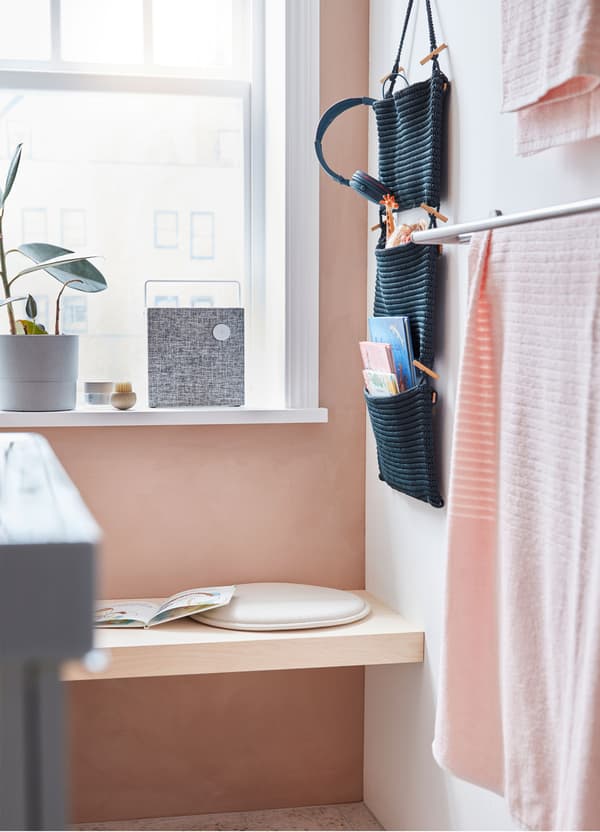 A small bench in a bathroom surrounded by NORDRANA woven blue hanging storage organisers and an ENEBY Bluetooth speaker.