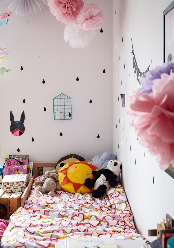 A small children’s bed, with bedlinen covered in hearts and soft toys.
