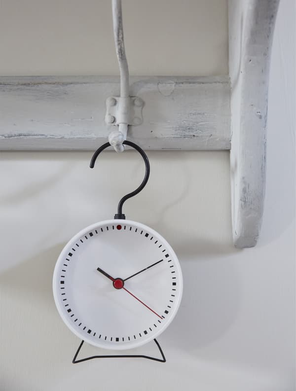 A small clock hanging on a painted coat hook.