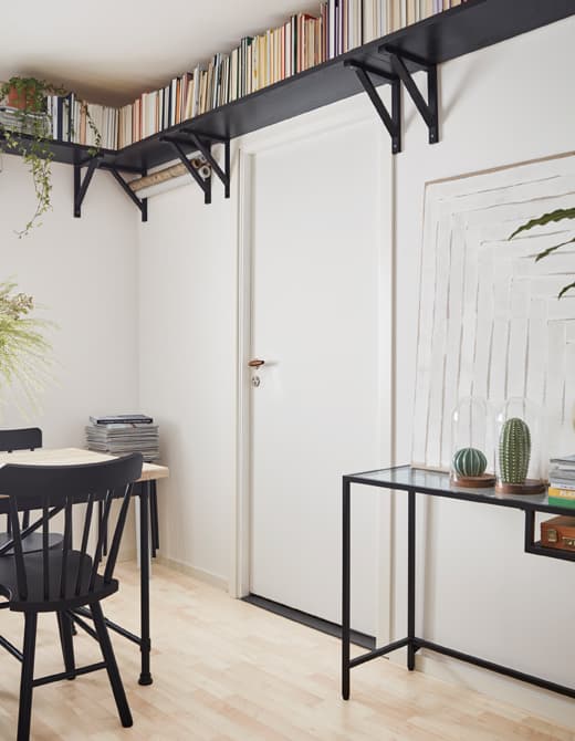A small dining room is decorated with a dining table and desk with long, thin legs, as well as book shelves up high along the ceiling.