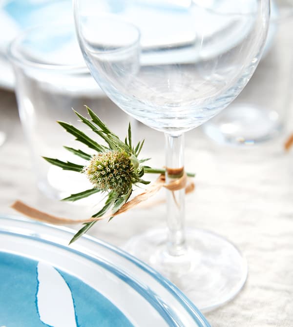 A small flower is tied to the stem of a red wine glass with twine.