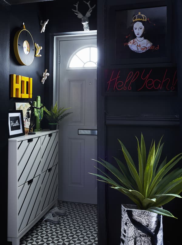 A small hallway with narrow shoe cabinets in white with black diagonal stripes, against black walls.