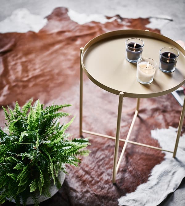 A small indoor fern next to a side table sitting on a cowhide rug.