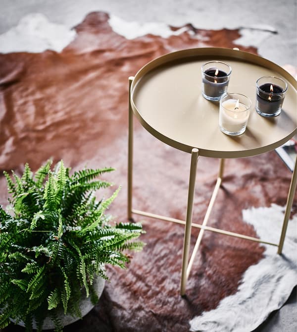 A small indoor fern next to a side table sitting on a cowhide rug.