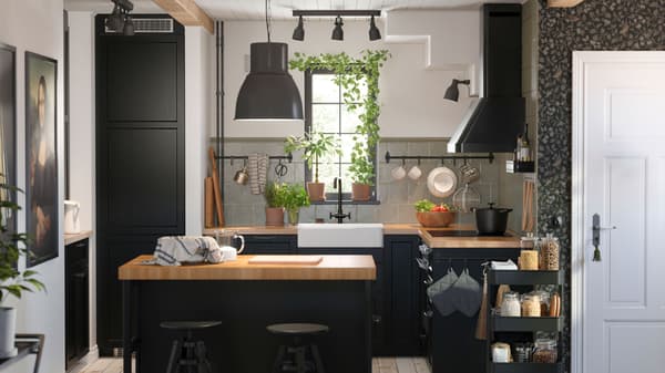 A small kitchen with LERHYTTAN black-stained fronts has a wooden worktop and a kitchen island with a black pendant lamp.