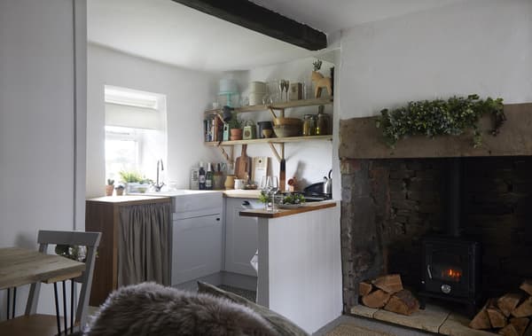 A small kitchen with open shelves above the worktop, next to a large fireplace.