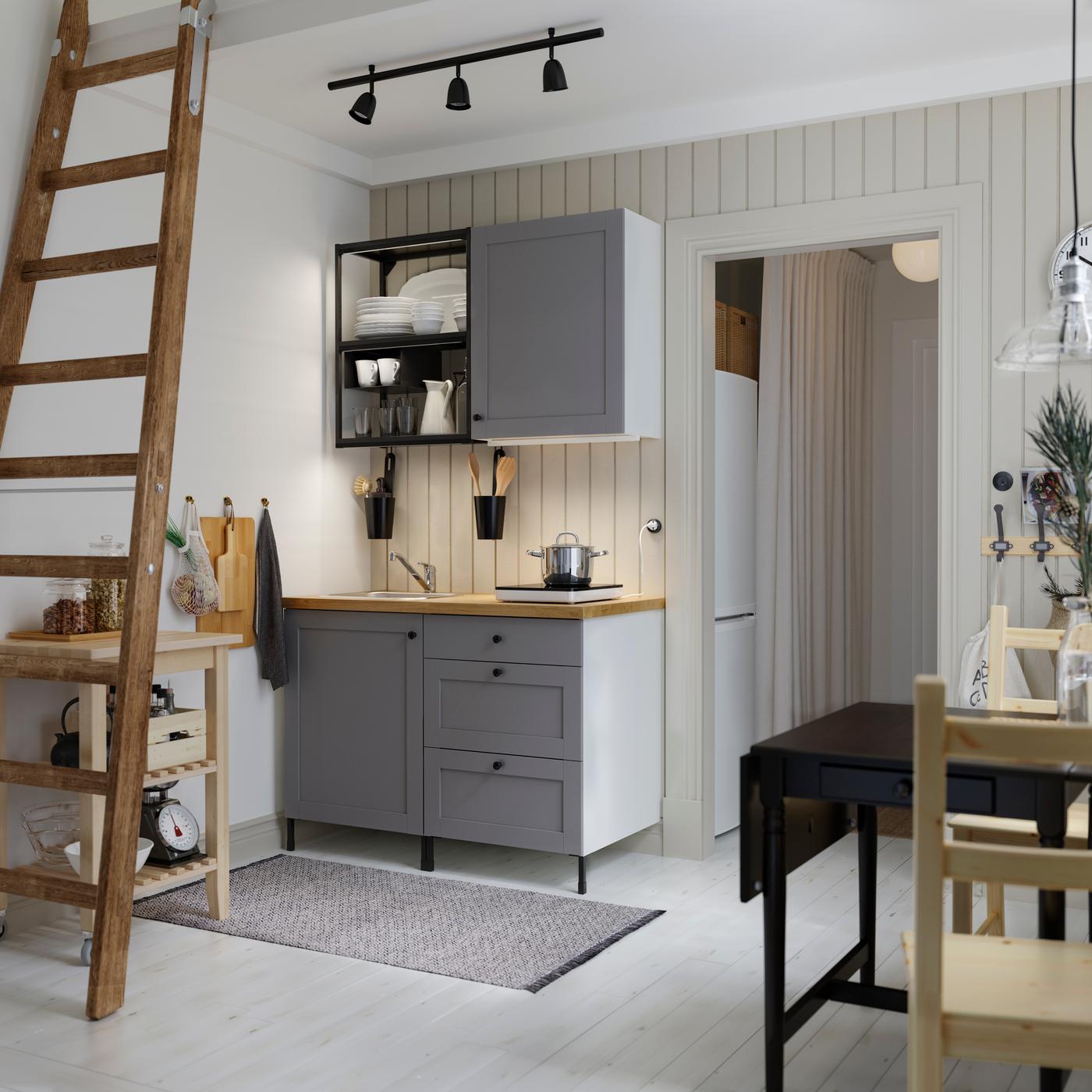 A small kitchen with open shelves in anthracite, grey fronts, a wood worktop, a black table and two wooden chairs.
