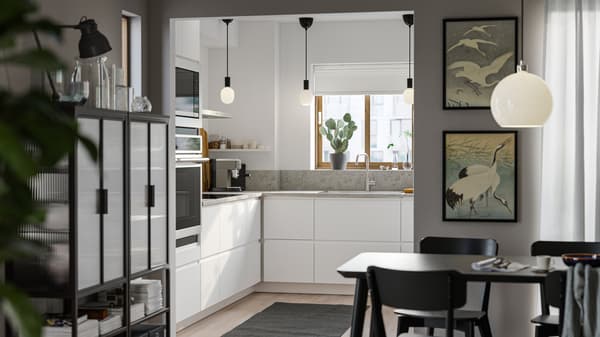 A small kitchen with smooth white VOXTORP fronts, white walls, a gray rug on the floor and three small black pendant lamps.