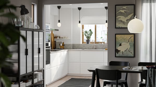 A small kitchen with smooth white VOXTORP fronts, white walls, a grey rug on the floor and three small black pendant lamps.