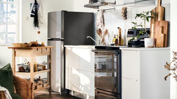 A small kitchen with white cabinet fronts, a top-freezer refrigerator, a white worktop and a wooden trolley.