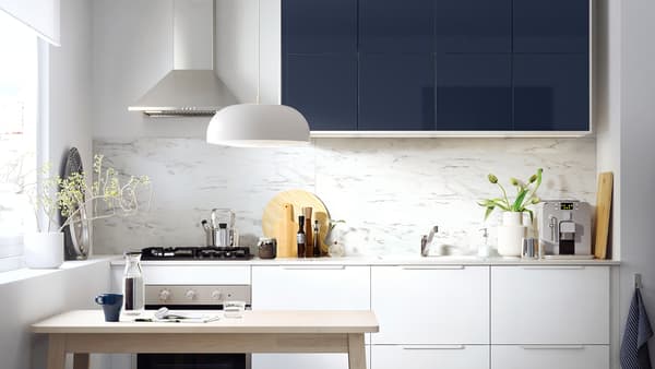 A small kitchen with white drawers and glossy black-blue kitchen cabinet fronts and a wooden table.