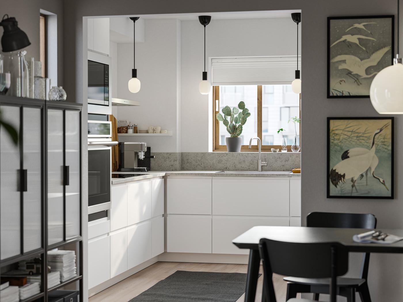 A small kitchen with white walls has smooth white VOXTORP fronts without handles and a dining area with darker furniture.