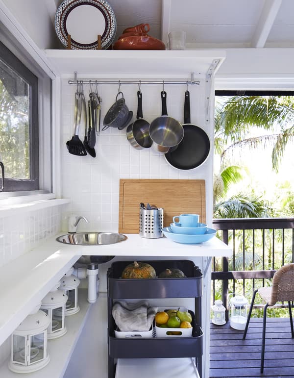 A small kitchenette consisting of a small round steel sink, a black trolley on wheels and a rail on the wall for utensils.