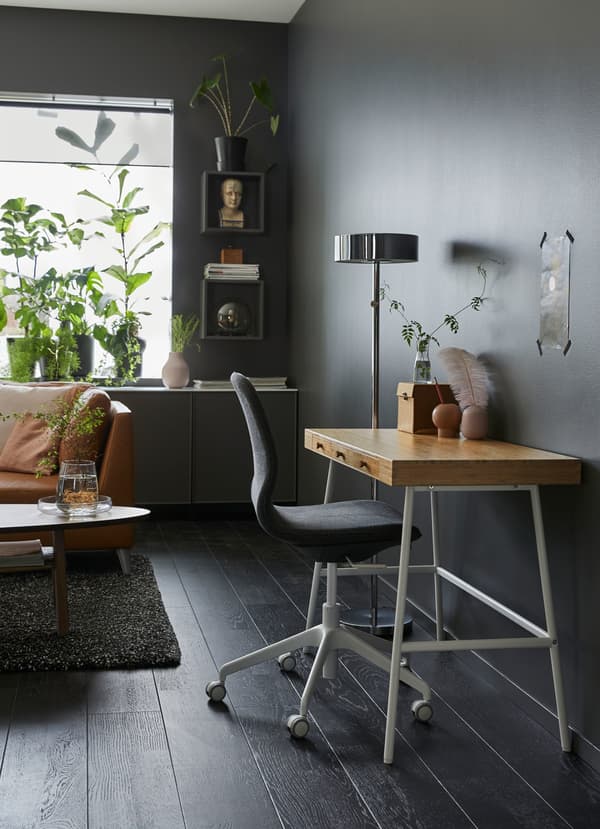A small LILLÅSEN work desk with a bamboo worktop surface and white legs against a dark grey sitting room wall.
