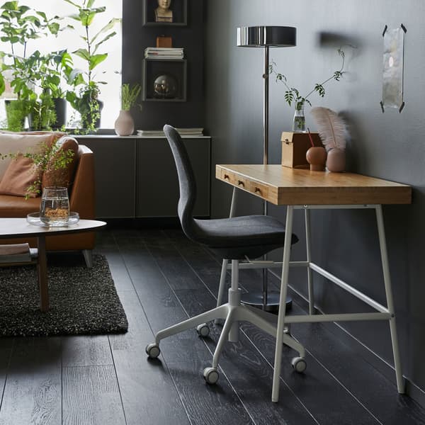 A small LILLÅSEN work desk with a bamboo worktop surface and white legs against a dark grey sitting room wall.