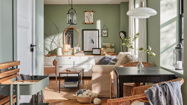 A small living room with green walls, a sofa, a small dining nook and framed posters and pictures on the wall.