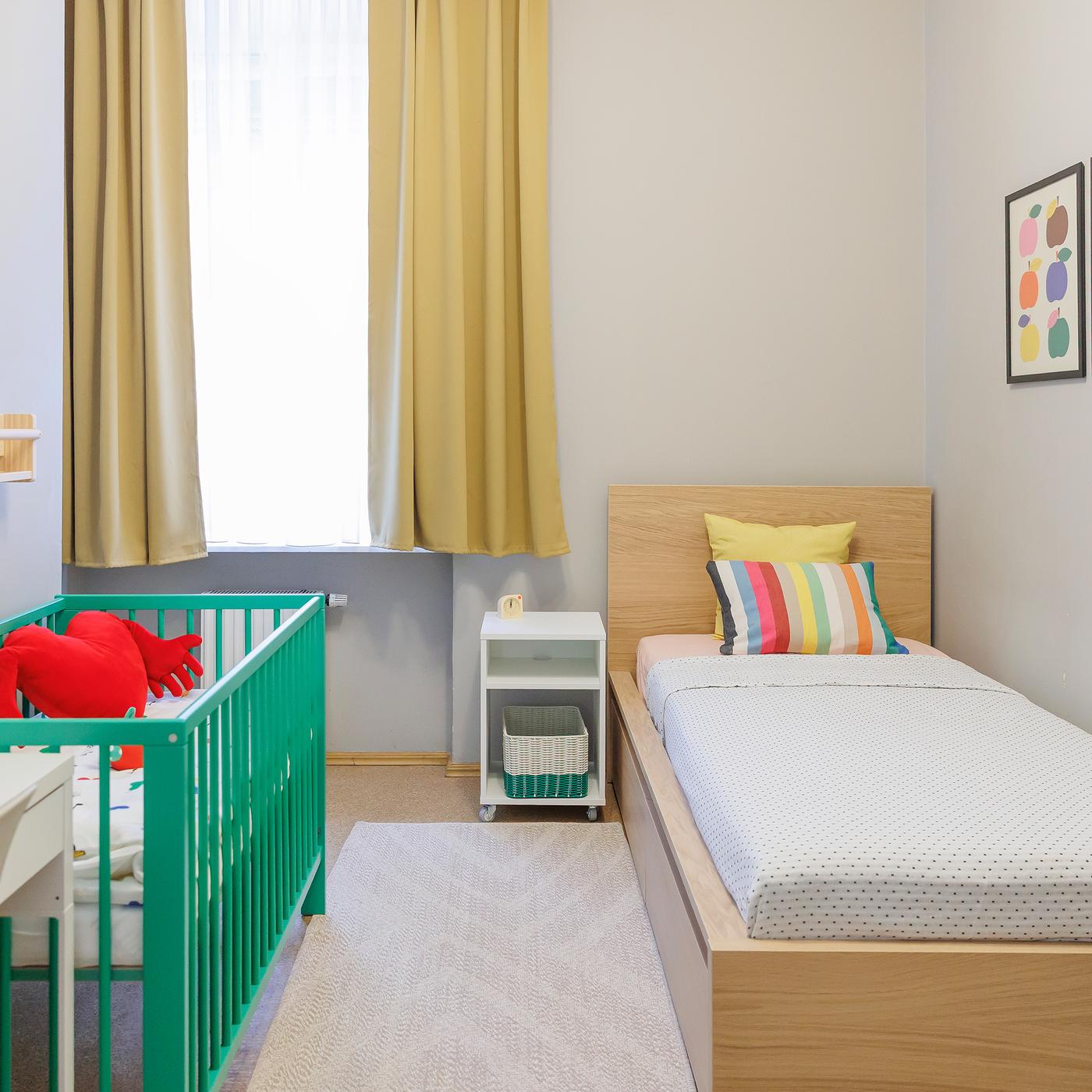 A small, neutral-toned family room with a single bed and a green baby cot.