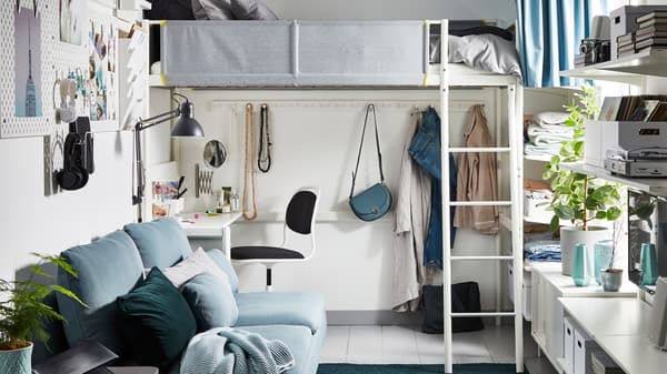 A small one bedroom home featuring a bunk bed with a workspace underneath, wall storage and a turquoise sofa.