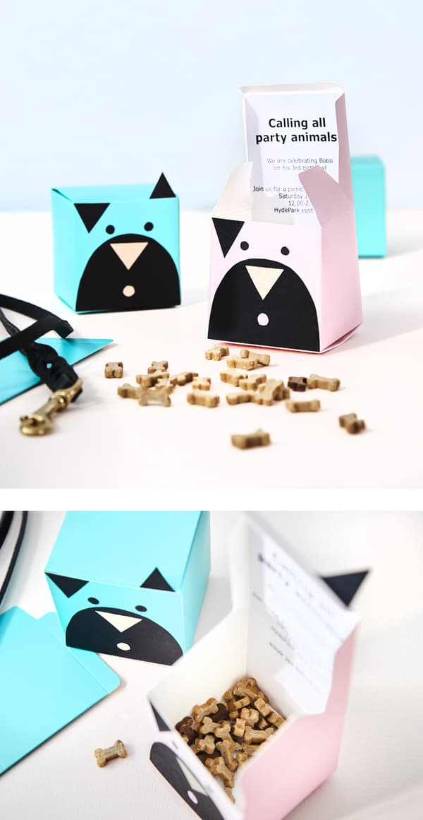 A small paper box is decorated with paper to look like a dog, and is filled with dog treats.