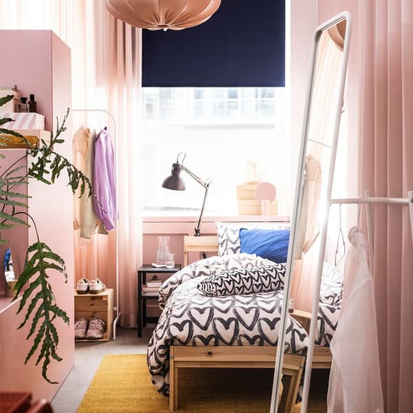 A small pink bedroom with a wood bedframe, a clothes rack and a standing mirror.