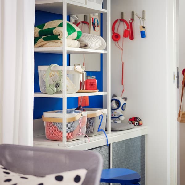 A small Scandi-style hallway has a white PLATSA open wardrobe with baskets and clothes on its shelves, against a blue wall.