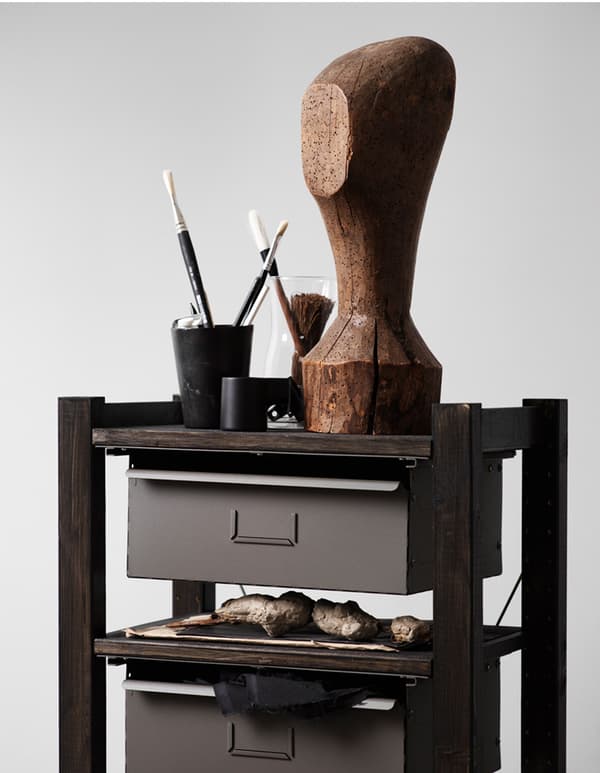 A small stained IVAR storage unit with drawers, topped with a sculpture and art material.
