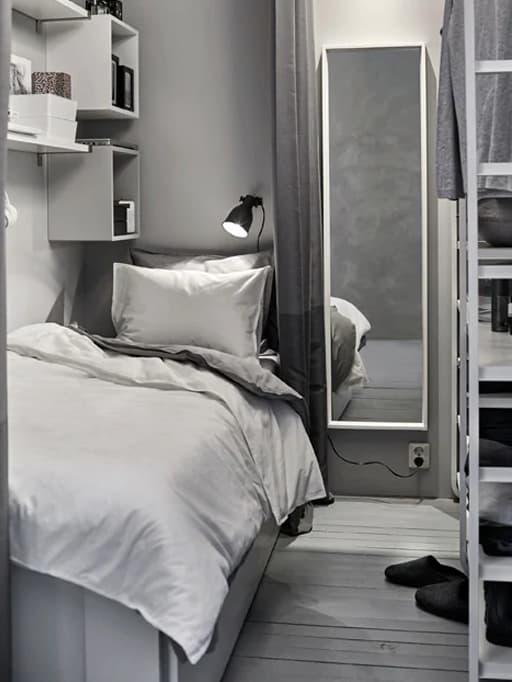 A small white and grey sleeping space is created in a shared space with a wardrobe.