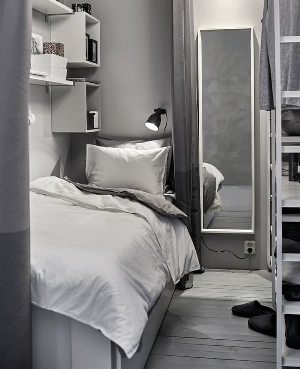 A small white and grey sleeping space is created in a shared space with a wardrobe.