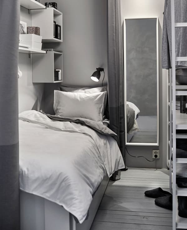 A small white and grey sleeping space is created in a shared space with a wardrobe.