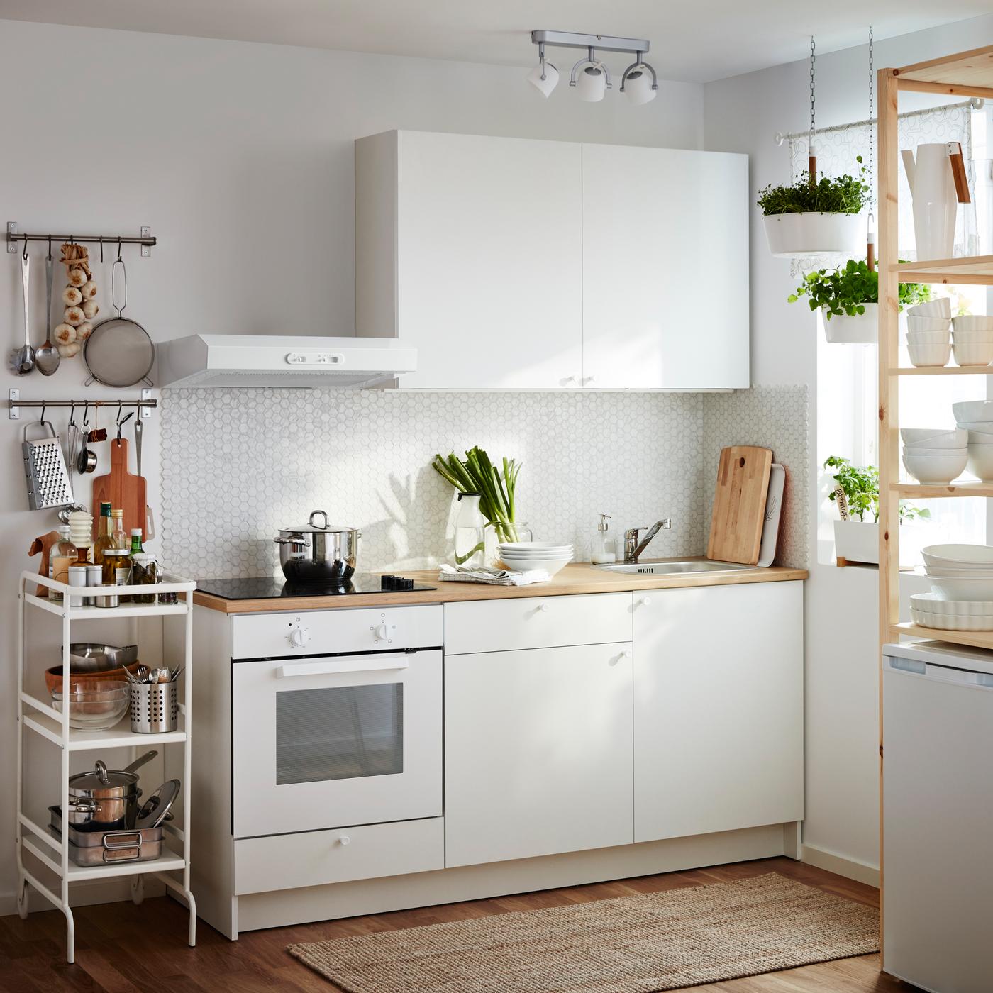 A small white kitchen consisting of a complete lower cabinet with doors, loaded, and an upper cabinet with doors. Combined with a white wall extractor, an oven and a black ceramic hob.