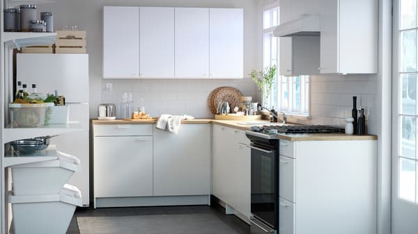 A small white kitchen with white base cabinets and white wall cabinets, white wall mounted shelves and a fridge/freezer.