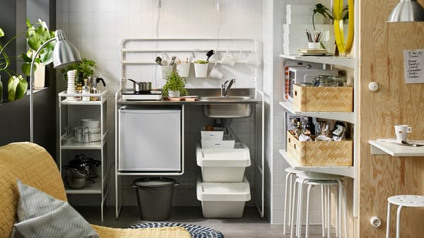 A small white mini-kitchen with a portable induction hob and a small fridge. A white trolley stores kitchen supplies.