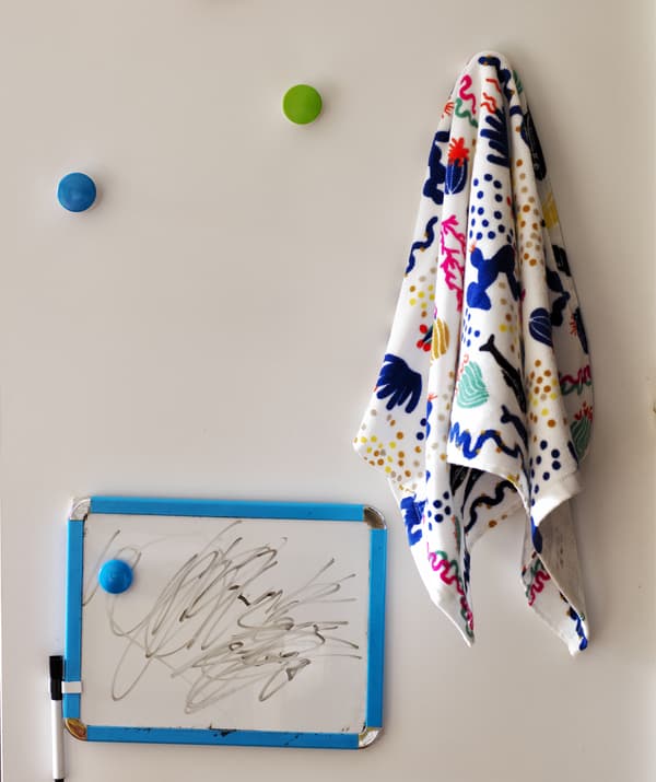A small whiteboard with pen and patterned material hanging on colourful hooks.