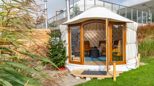 A small yurt with an open door and cosy armchairs inside stands on the lawn