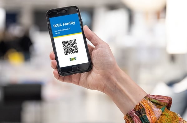 A smartphone held in a person's hand. The screen shows an IKEA Family digital membership card with a QR code, the IKEA logo, and the member's email address.